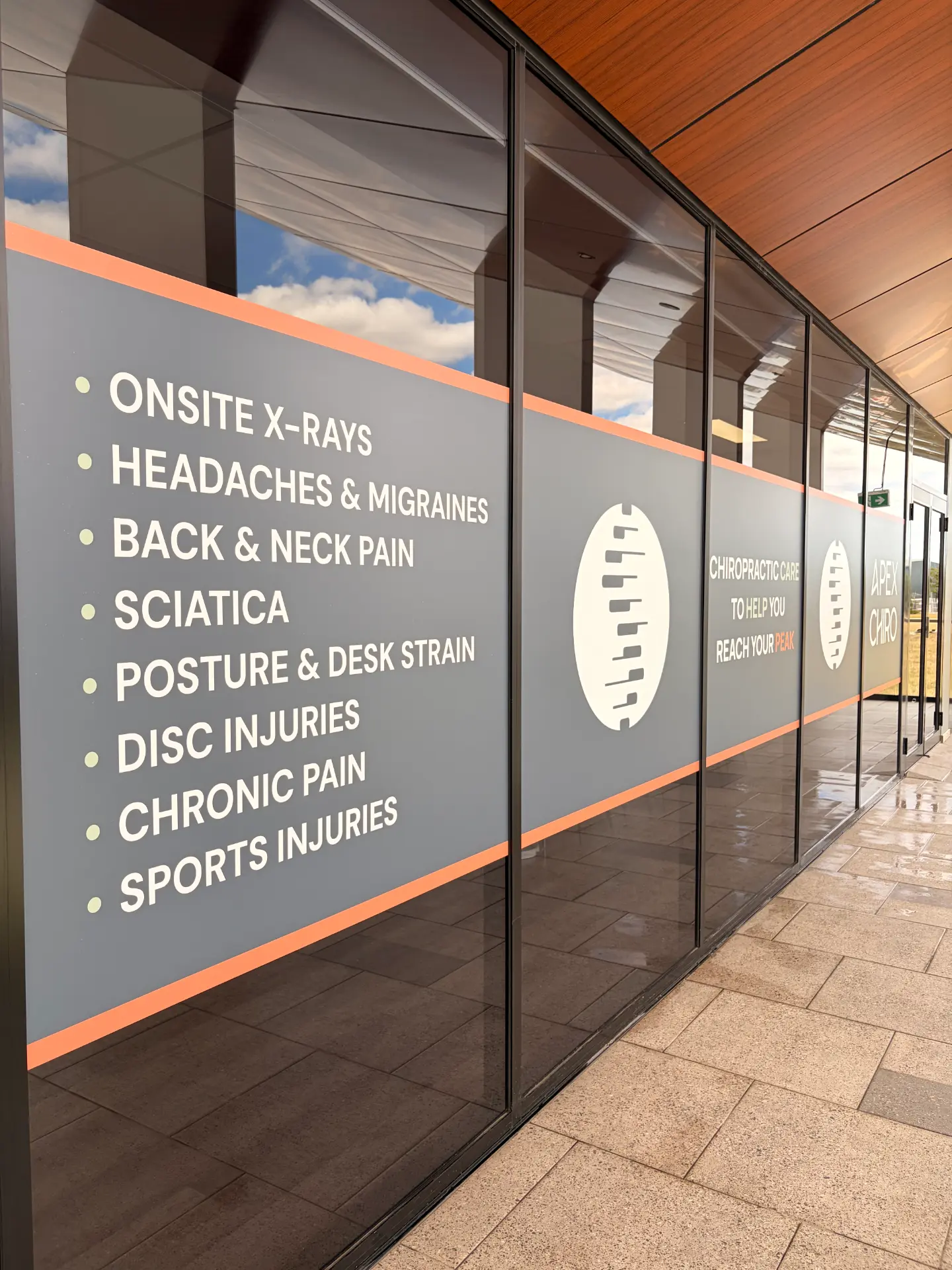 APEX. Chiro Gregory Hills clinic signage at The Hub Gregory Hills listing conditions treated including back pain, sciatica and headaches